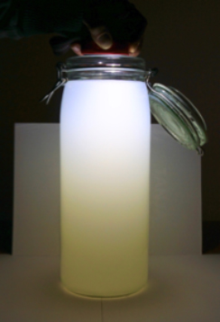 Glas mit Wasser und Milch, von oben wird mit einer Taschenlampe reingeleuchtet. Oben scheint das Licht blau, unten gelb.